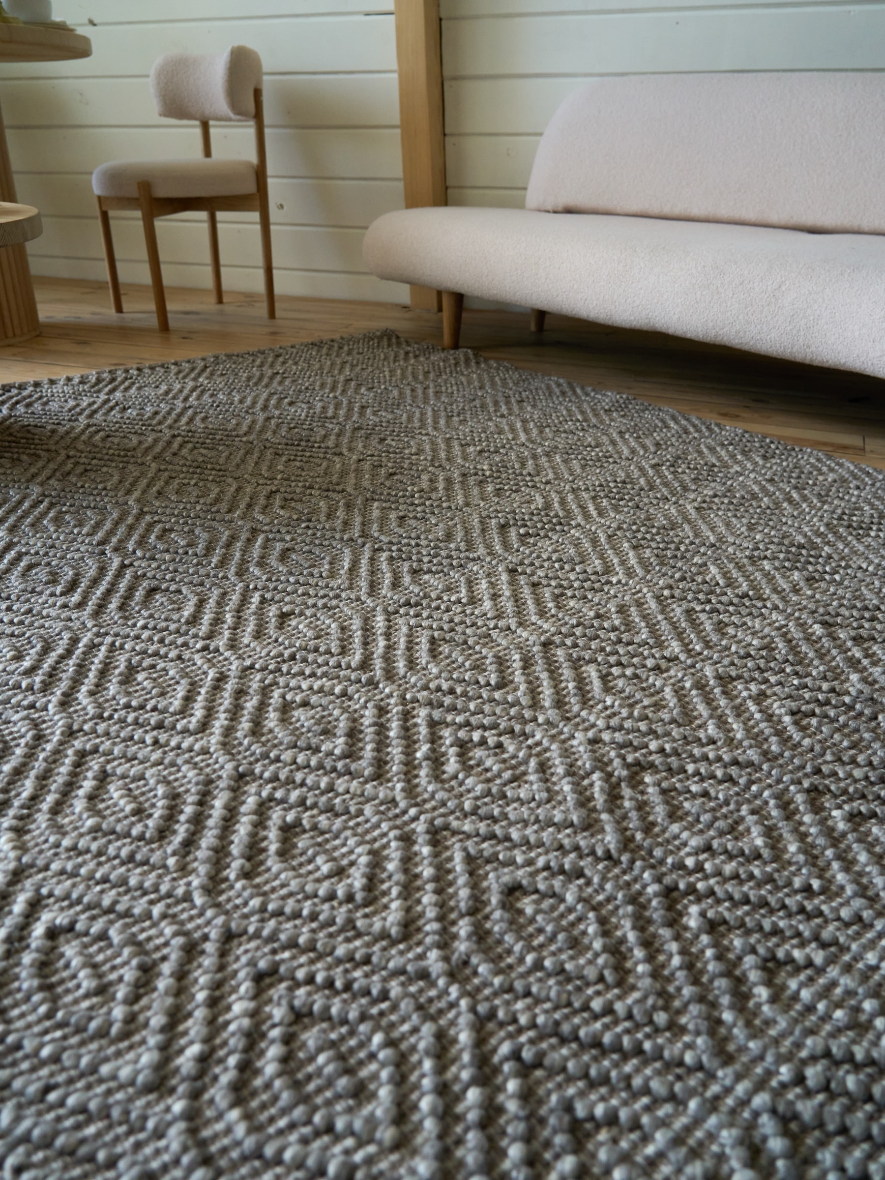 Grey patterned rug on a wood floor beside a light sofa and round table.