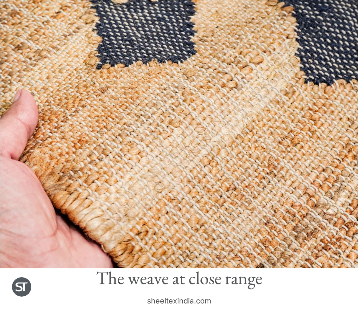 Close view of cream, honey and tan crossing threads beside a dark diamond-shaped motif, with a hand holding the rug edge.