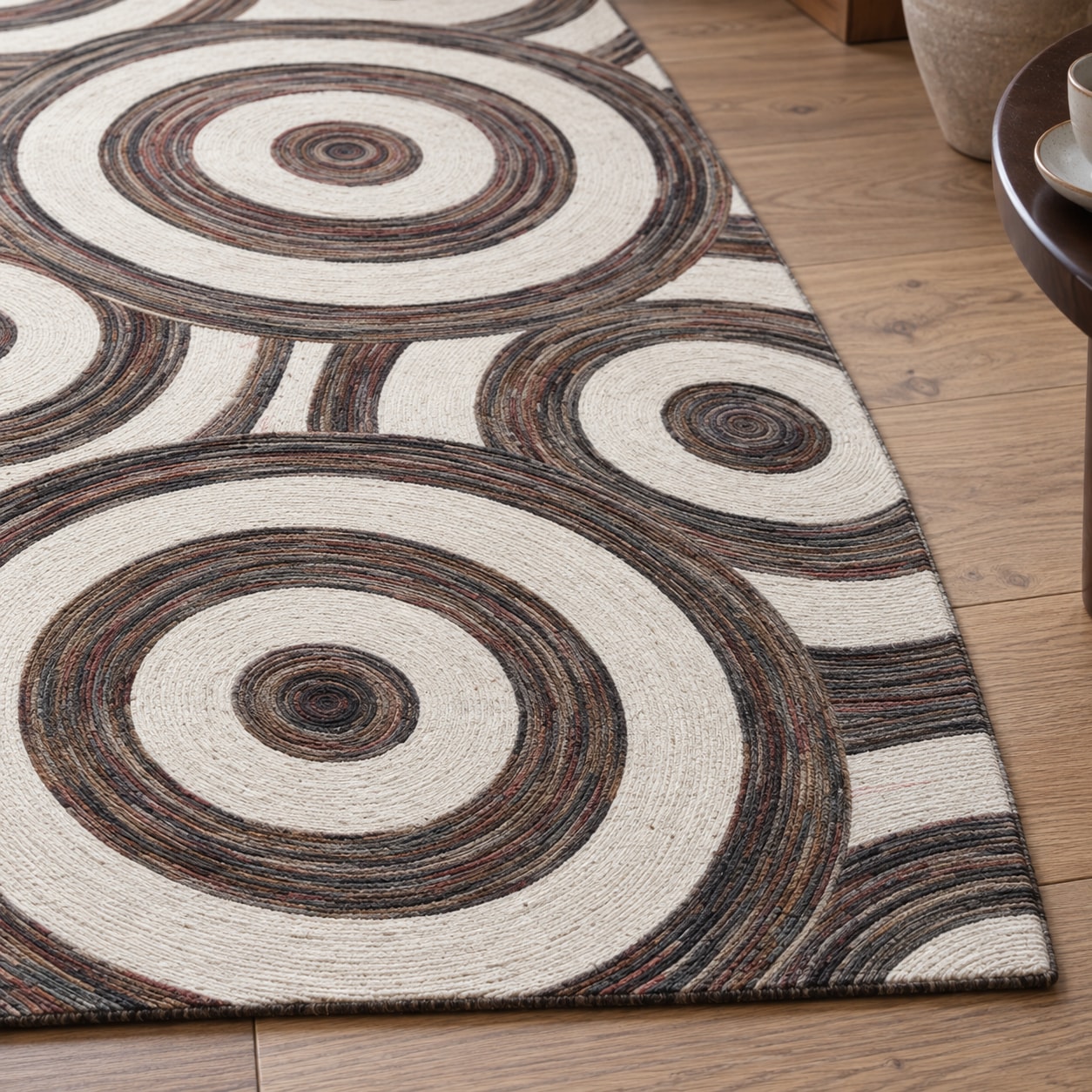 Close view of a cream wool carpet with broad brown and taupe rings beside a wooden floor.
