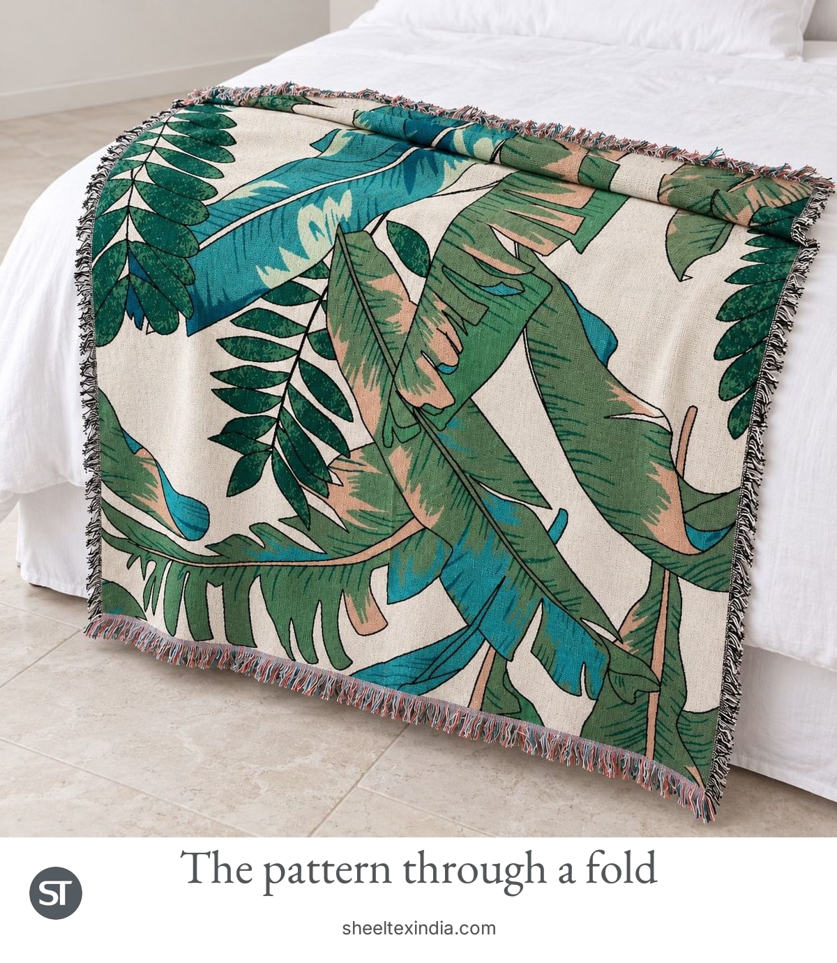 Green and teal leaf-pattern throw draped over a white bed with its top edge folded back and fringe visible.